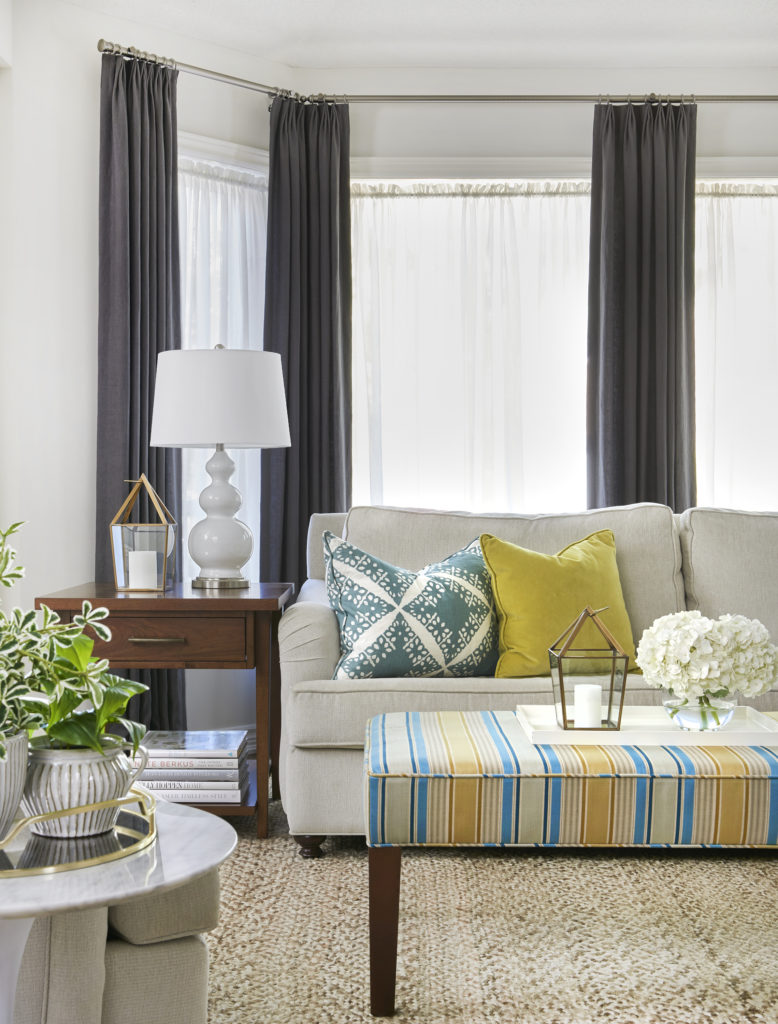 Light and bright living room with a neutral sofa, colorful pillows, and a striped ottoman
