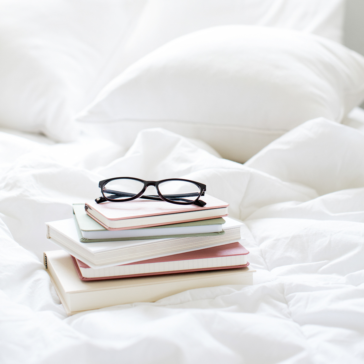 bed with white bedding and a stack of books with reading glasses on top