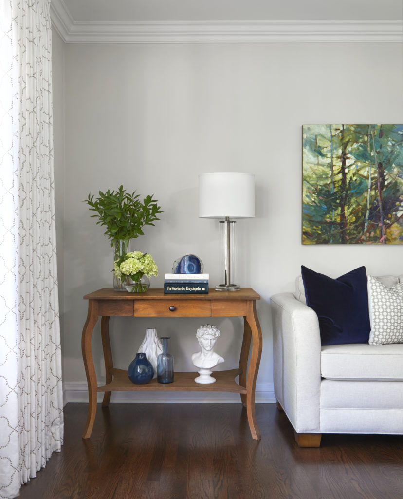 corner of bright living room with an antique table styled with home decor accessories, flowers, and a lamp