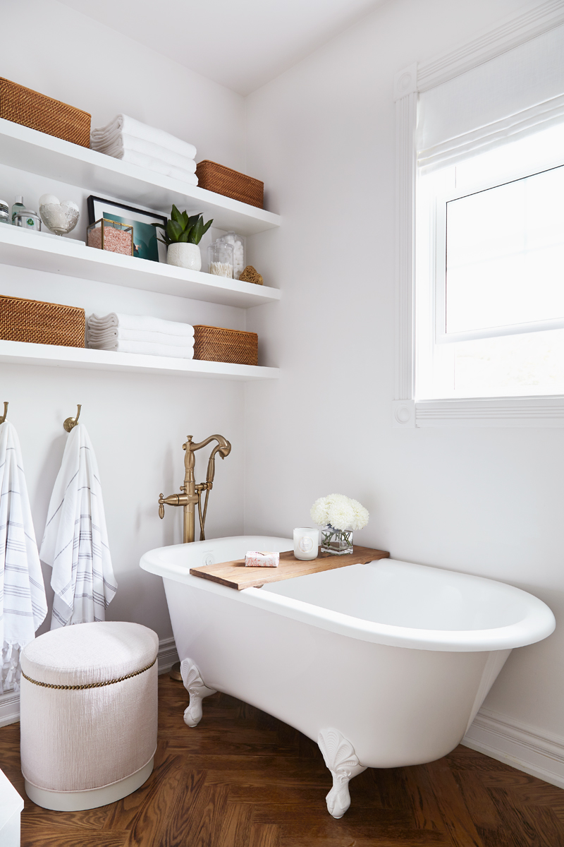 white bathroom with clawfoot tub, stool, and beautifully styled floating shelves