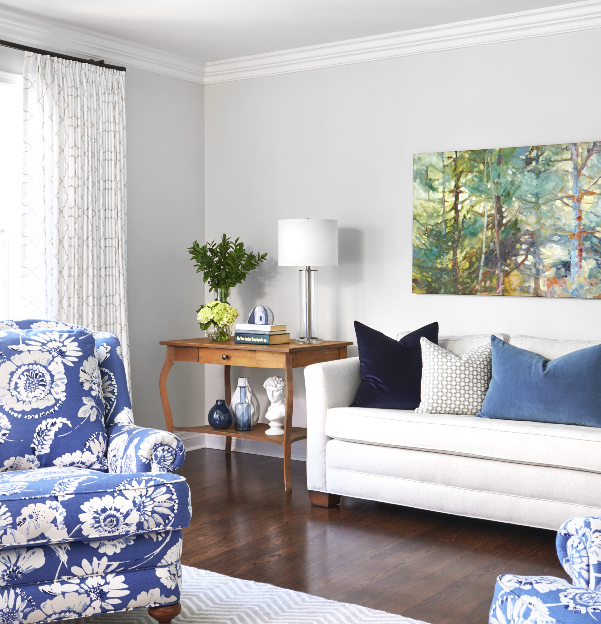 corner of bright living room with a sofa that is layered with blue pillows, and antique side table next to it, and original hanging artwork above