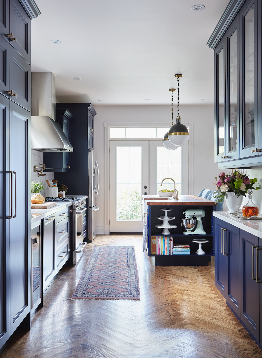 beautiful kitchen with herringbone wood floors, blue cabinets, and white walls