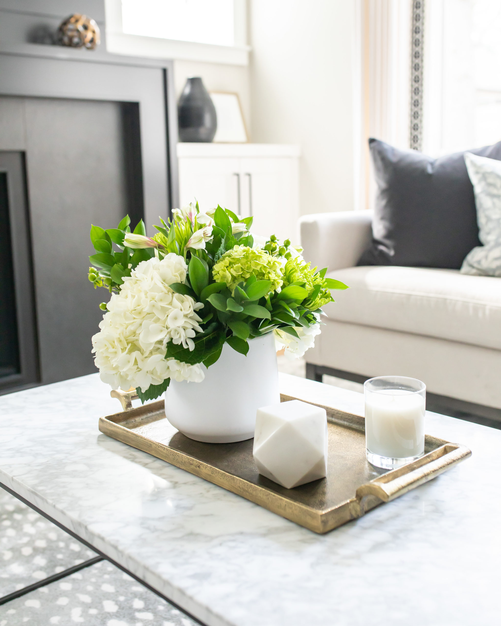 white marble coffee table with gold tray, flowers in white pot, and marble decorative object and candle