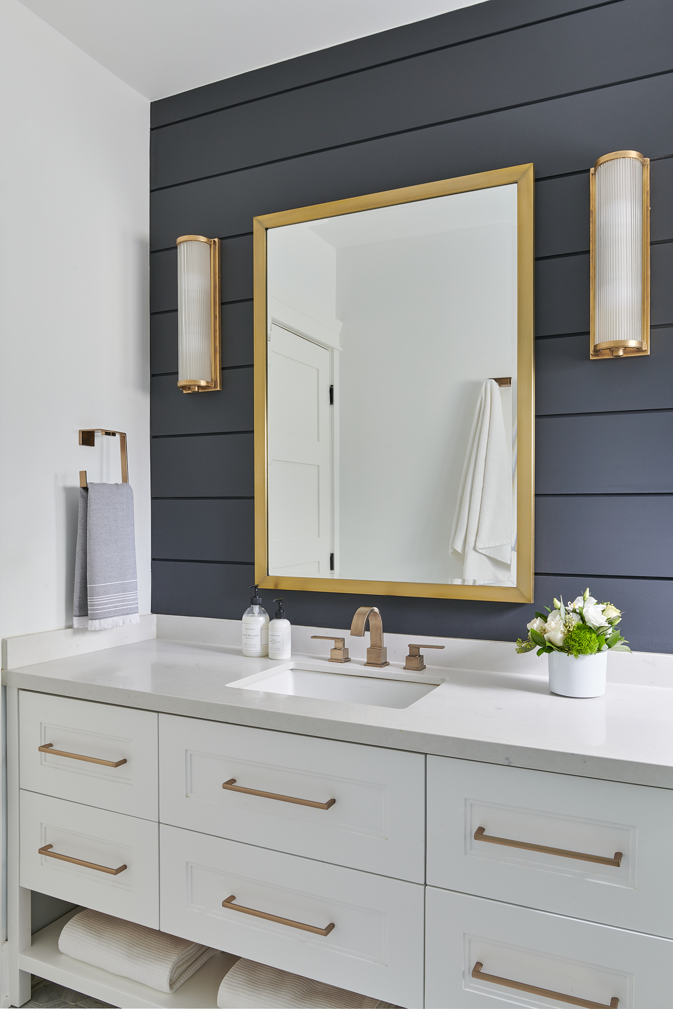 custom bathroom design with white vanity, gold hardware, mirror, and wall sconces, all on a striking black shiplap wall