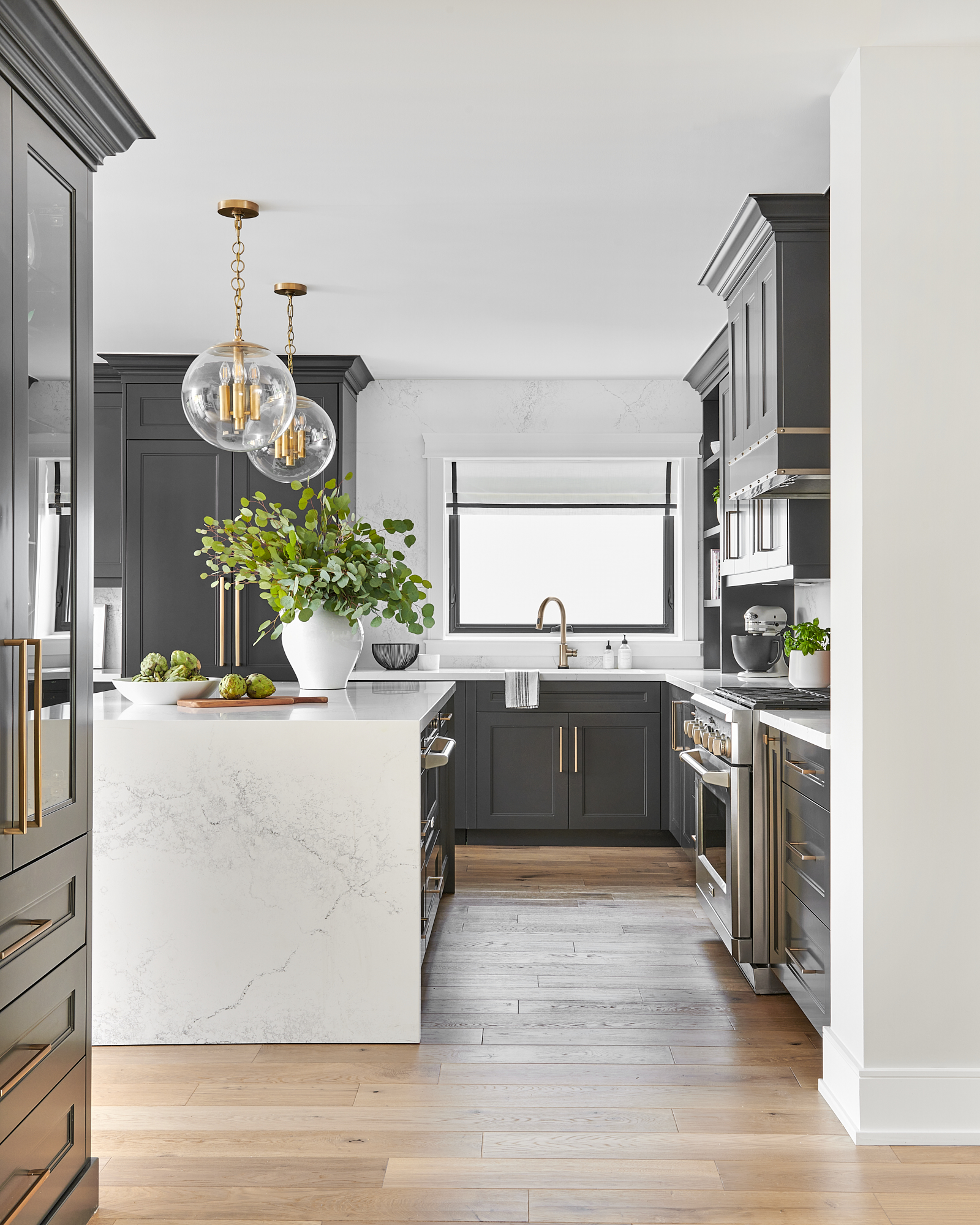 beautiful custom kitchen with white oak hardwood floors, stone waterfall countertop on island, dark grey cabinets and gold hardware