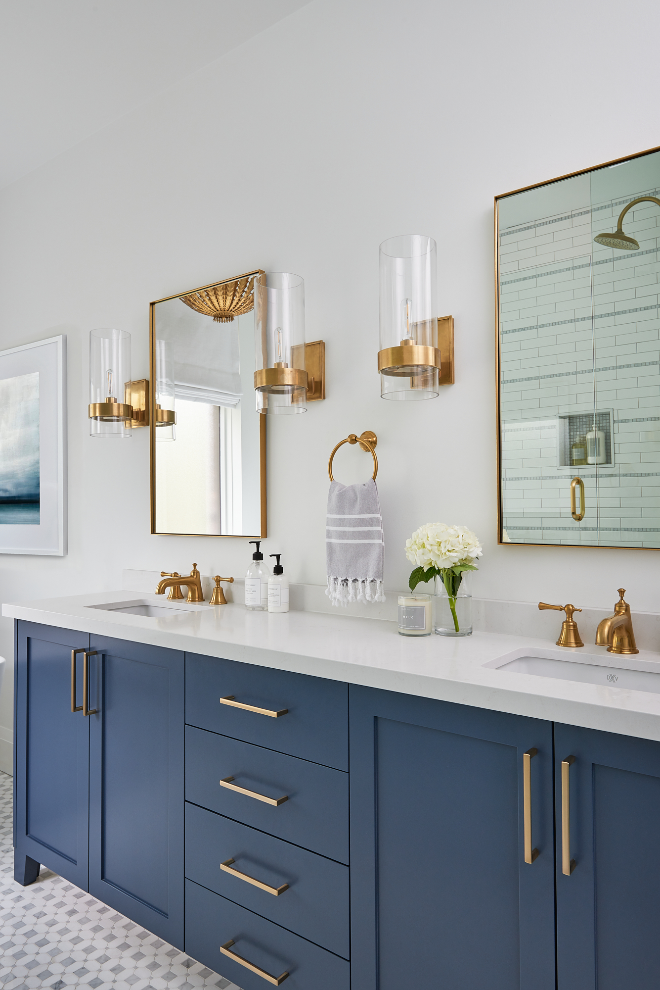 custom vanity with blue cabinets, gold fixtures, and decorative wall sconces on either side of mirrors