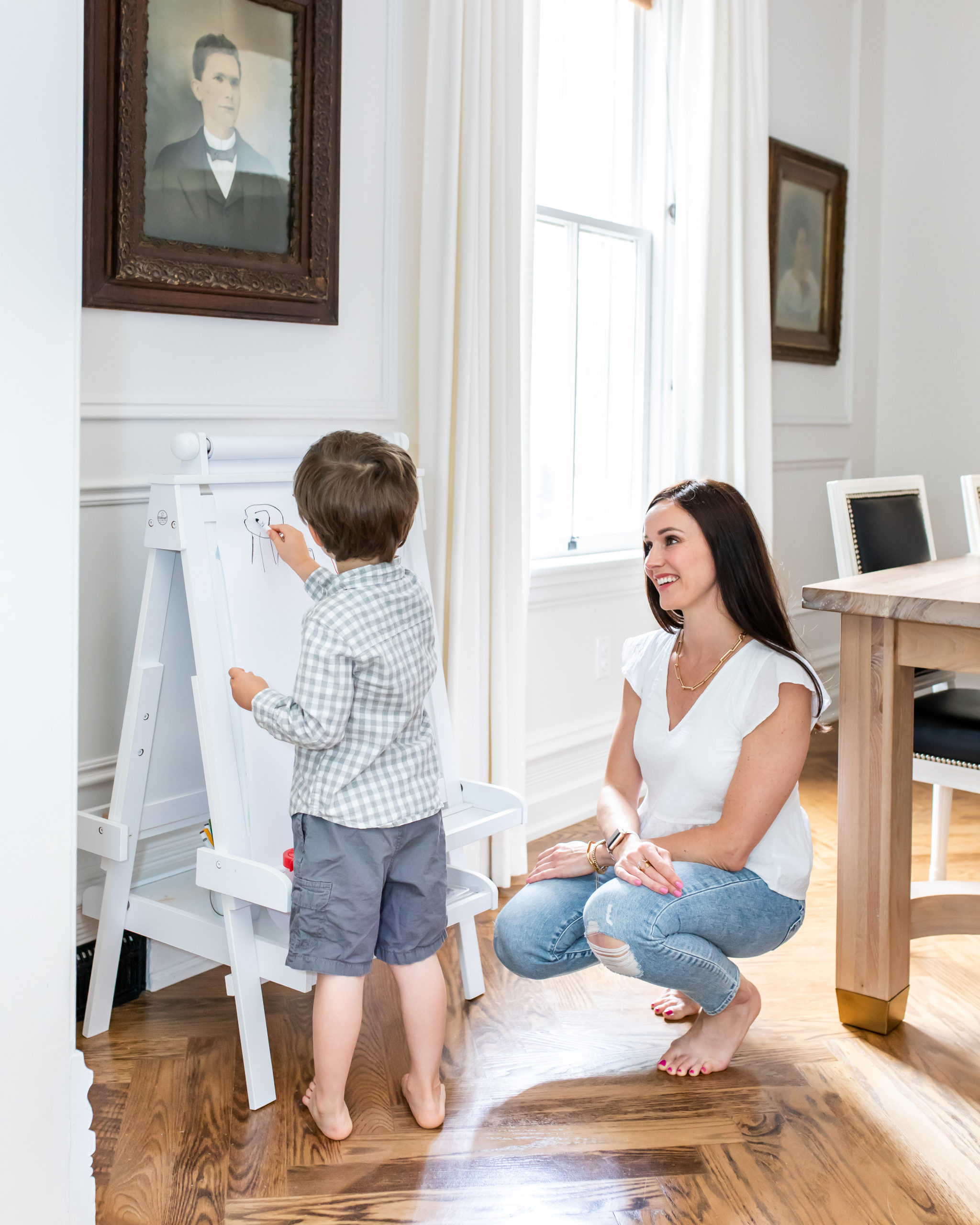 Interior Designer Staci Edwards kneeling down with son as he colours at his easel in their dining room