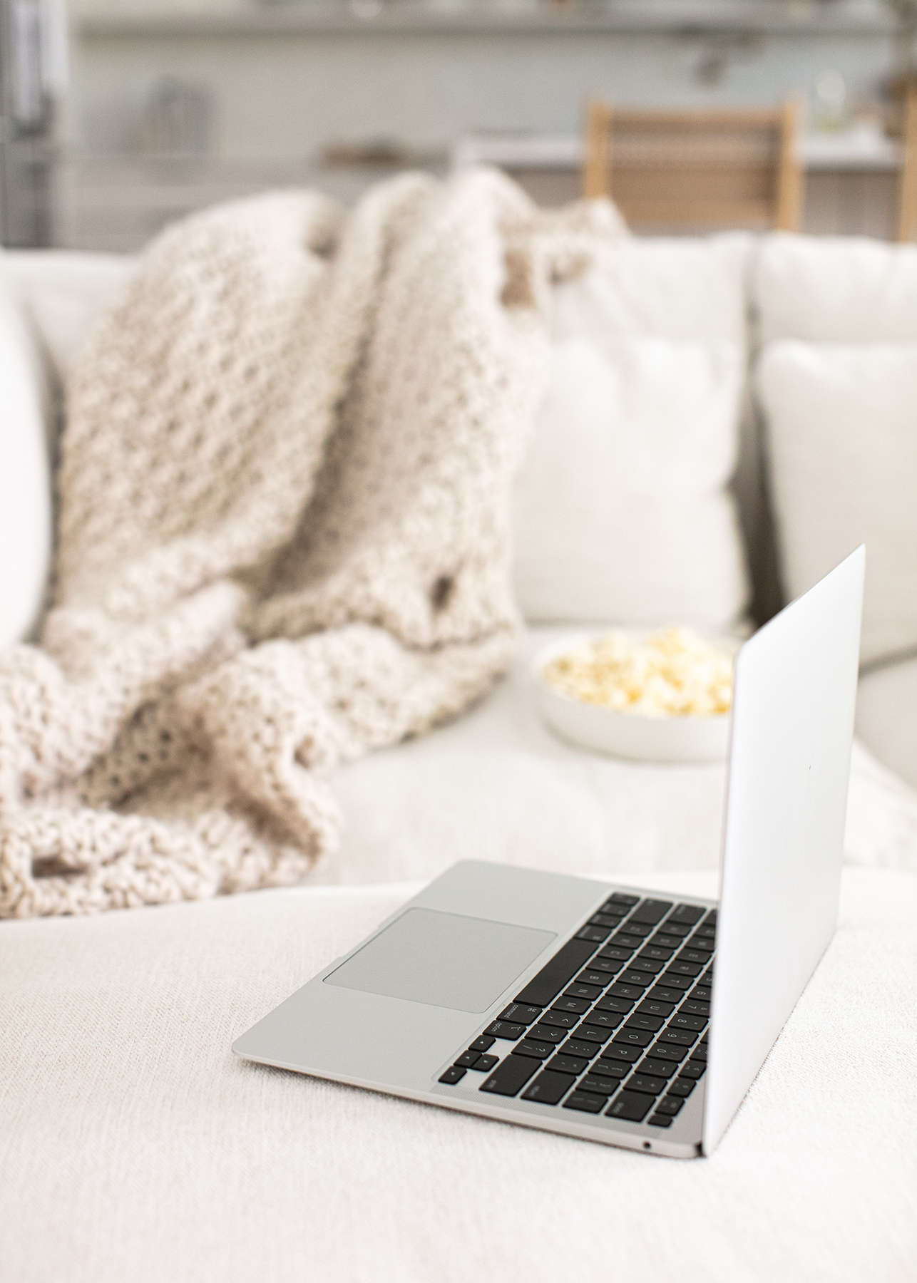 comfortable sofa with laptop and a bowl of popcorn set on the seat and a thick knit blanket draped over the back