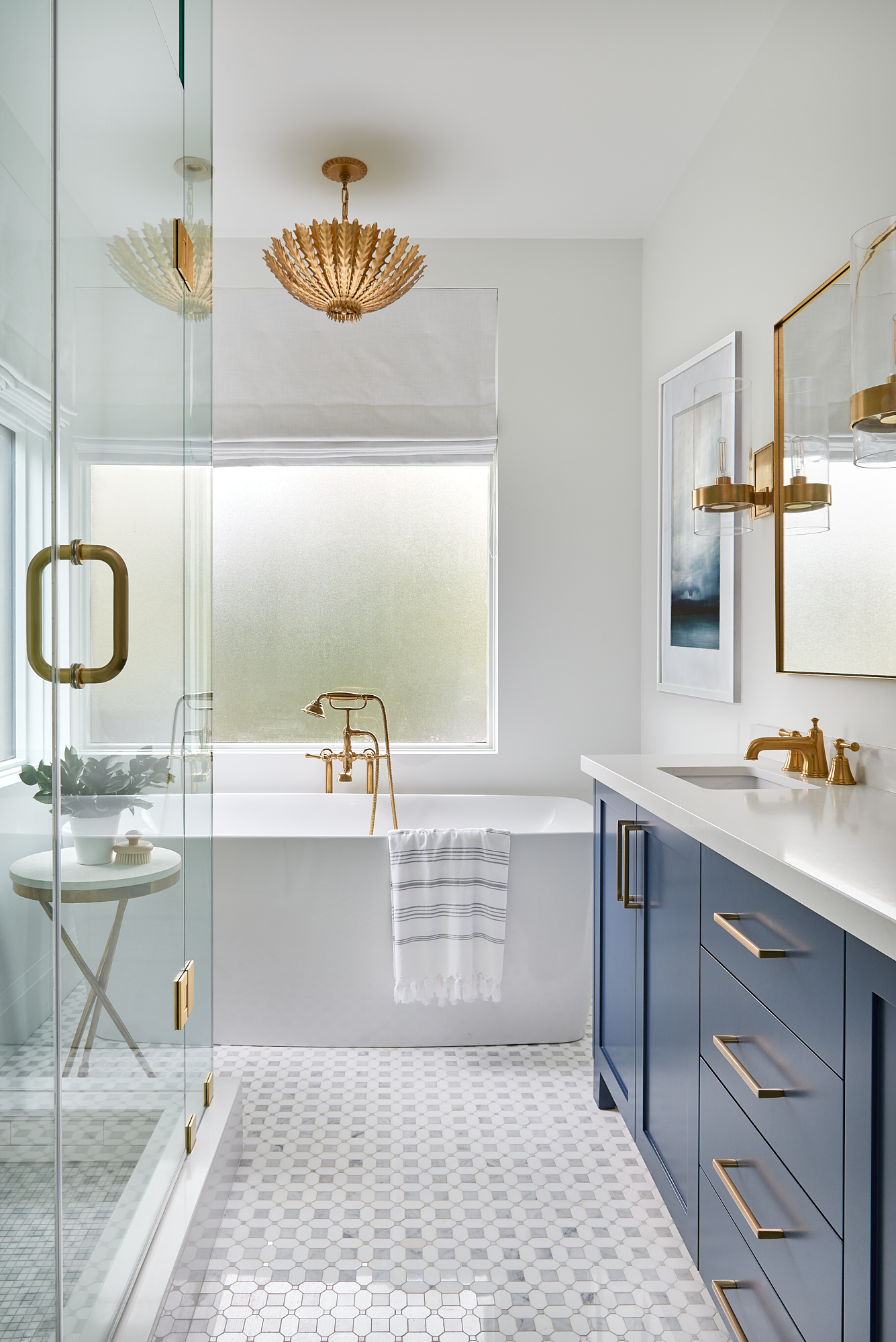 toronto bathroom after renovation by interior designer staci edwards with white walls, blue vanity, gold hardware, and beautiful light fixture above the bathtub