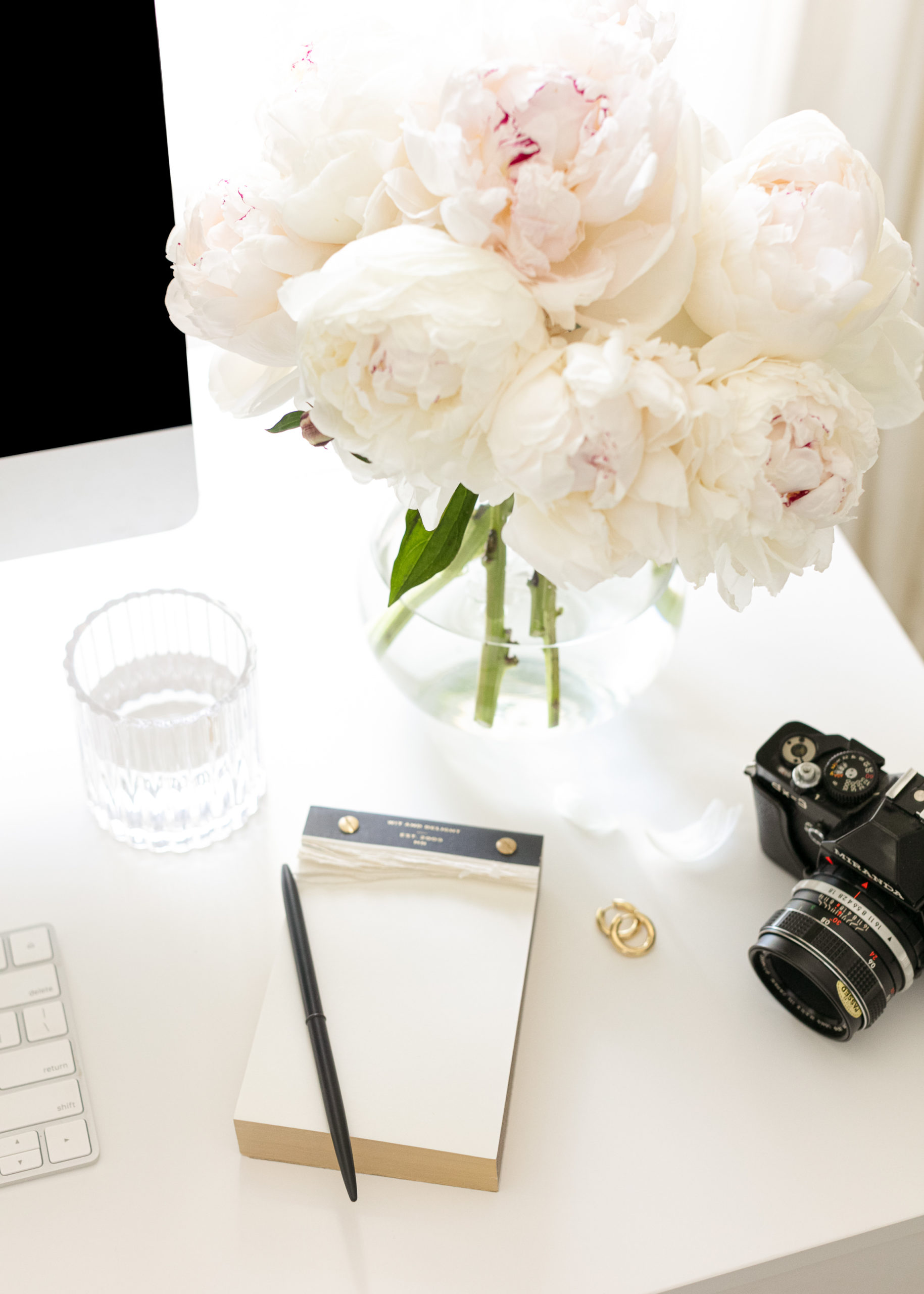desk with a note pad, glass of water, vase of flowers and a camera