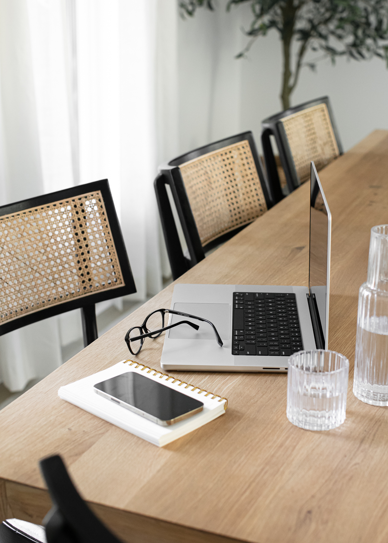 photo of interior designer's work area with laptop, glasses, iphone, and a glass of water with pretty black and cane chairs in the background