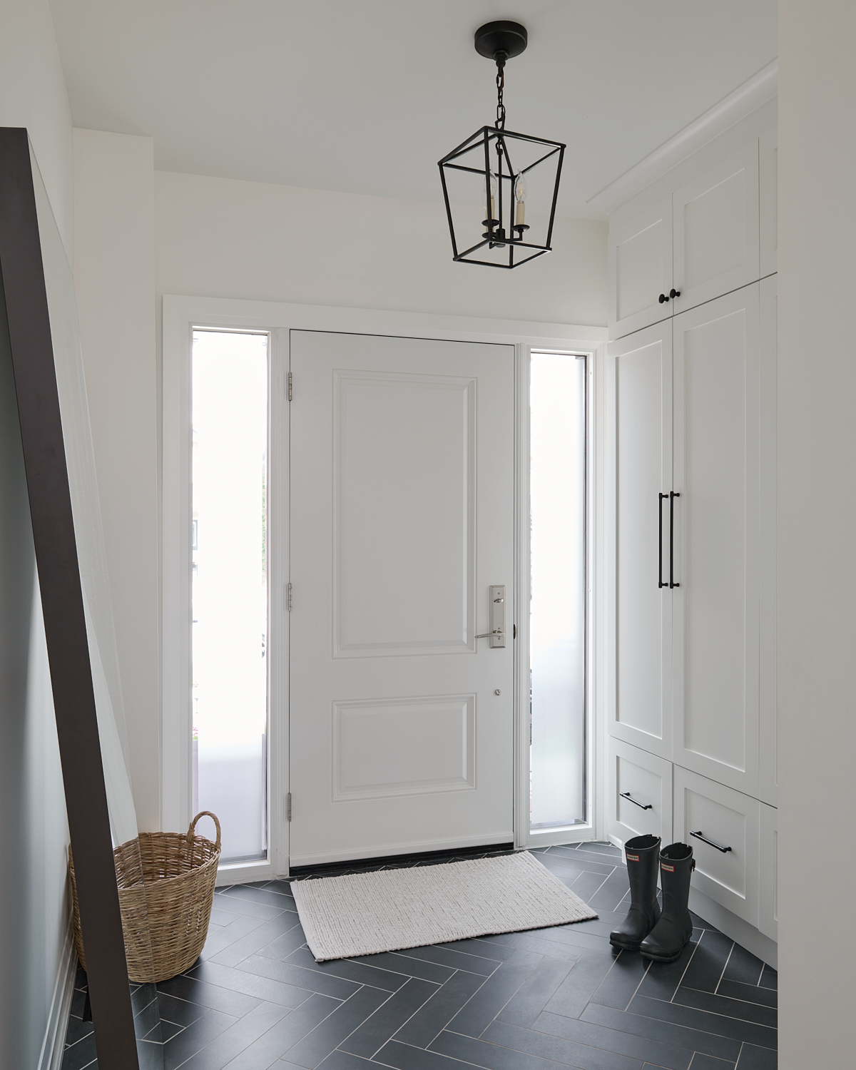 Foyer with white walls and cabinetry and dark herringbone tiled floors