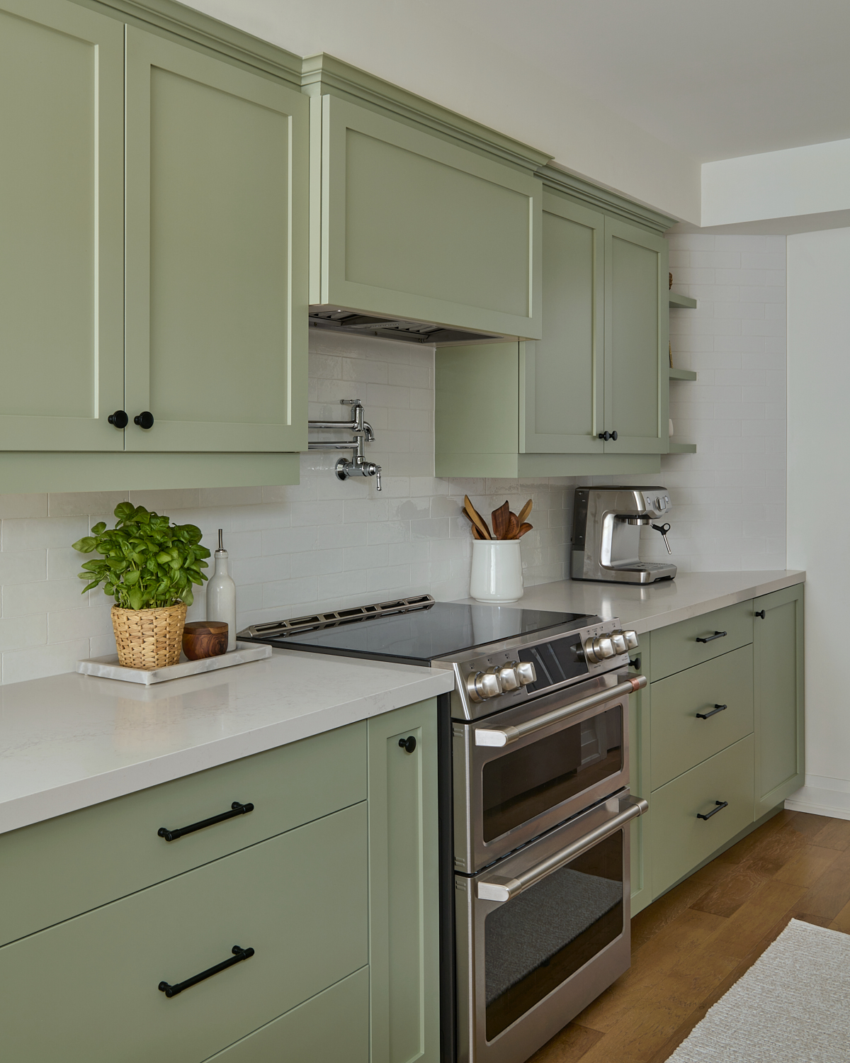 kitchen with light green cabinets, oak wood floors, white countertops and tiled backsplash
