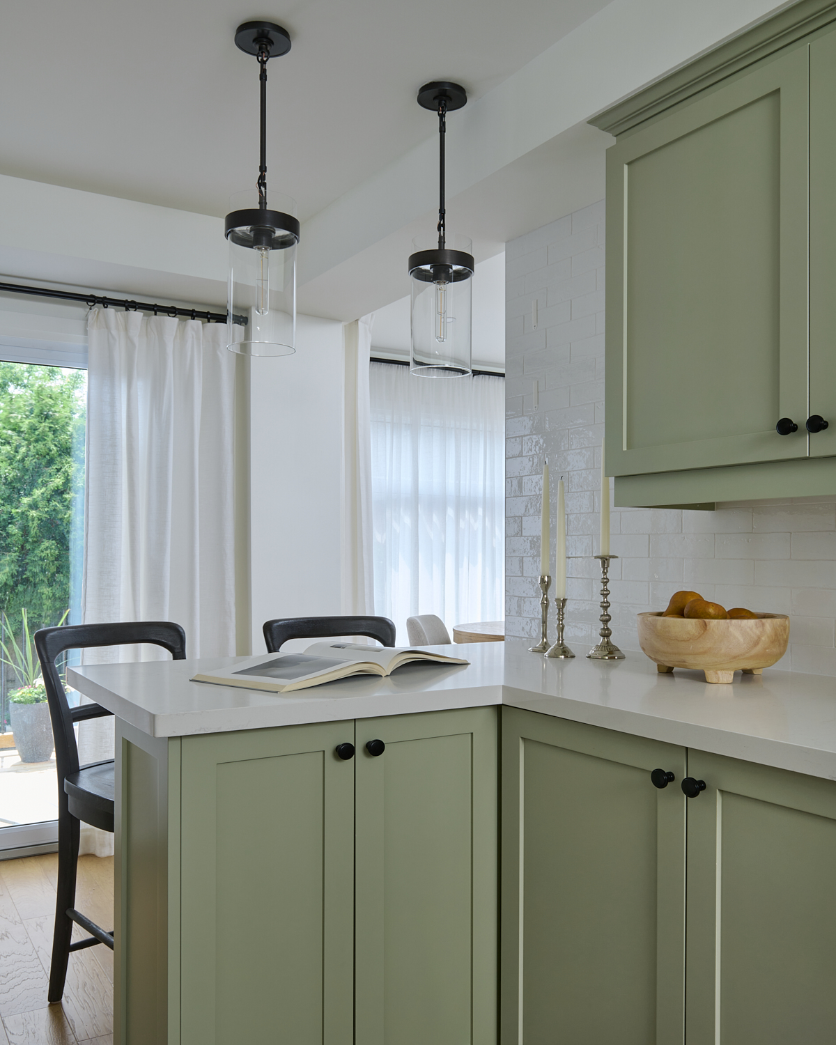 kitchen with light green cabinets, oak wood floors, black pendant lights, white countertops and tiled backsplash