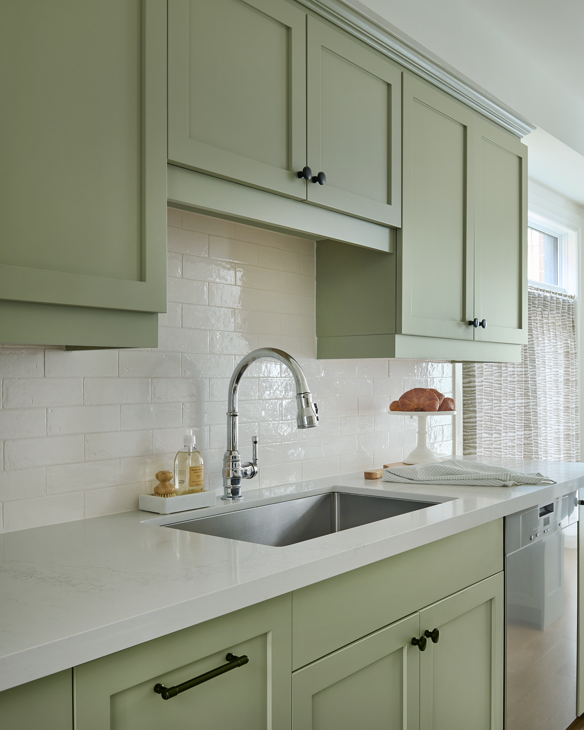 kitchen with light green cabinets, oak wood floors, pretty chrome faucet, white countertops and tiled backsplash