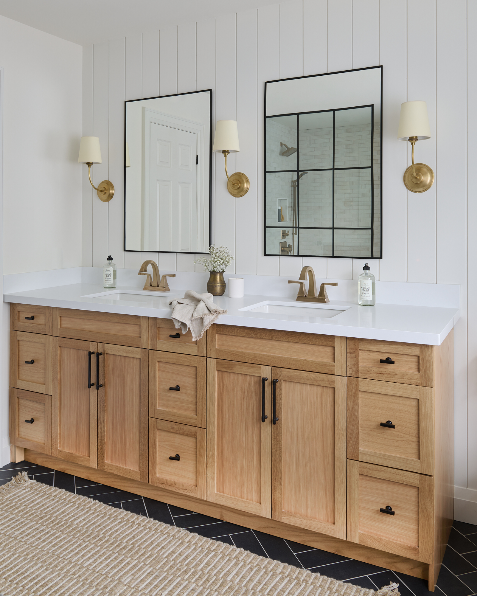 bathroom interior designed with oak wood vanity, nickel gap wall detail, gold plumbing fixtures and decorative sconces 