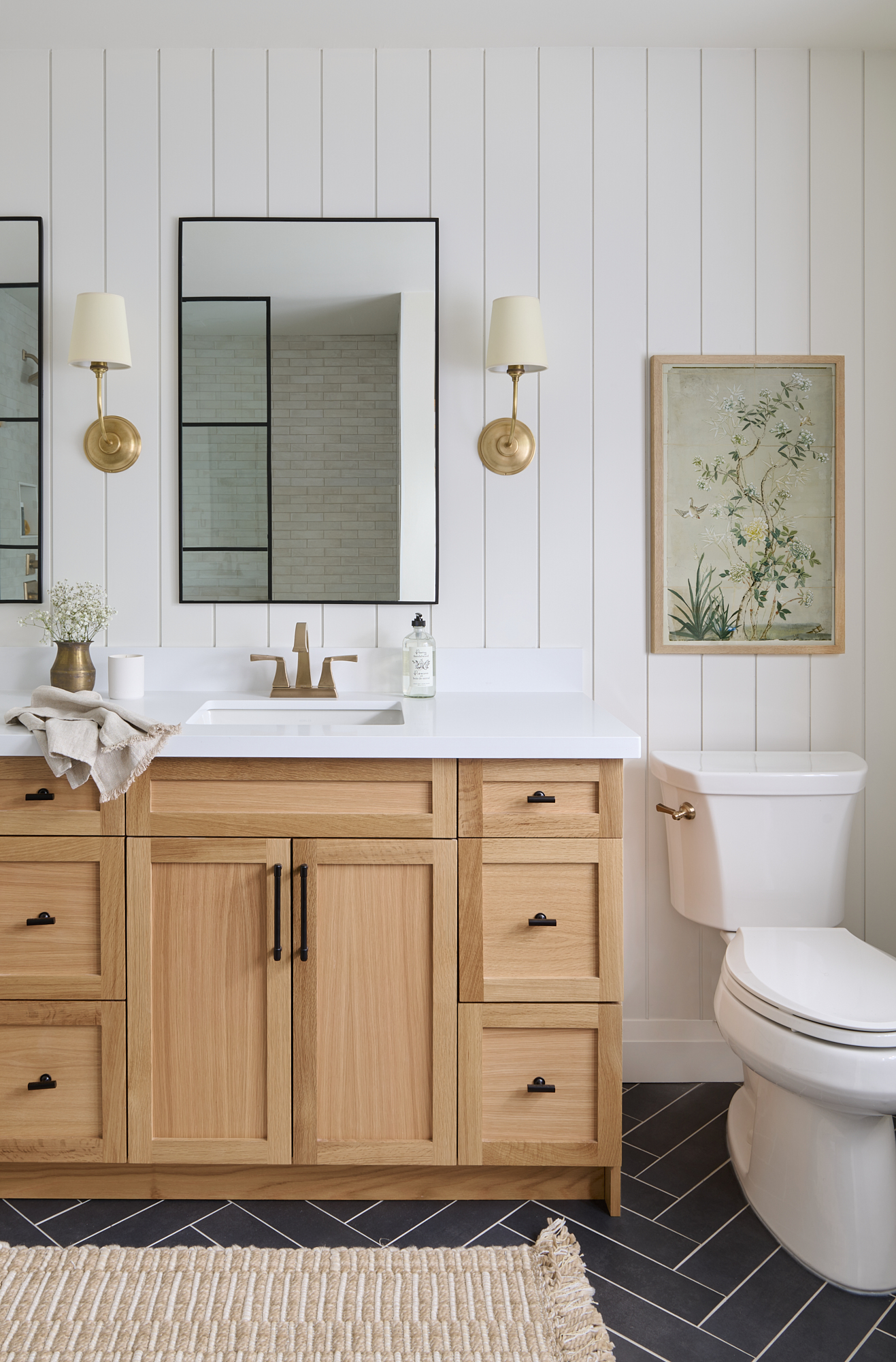bathroom interior designed with oak wood vanity, nickel gap wall detail, gold plumbing fixtures and decorative sconces