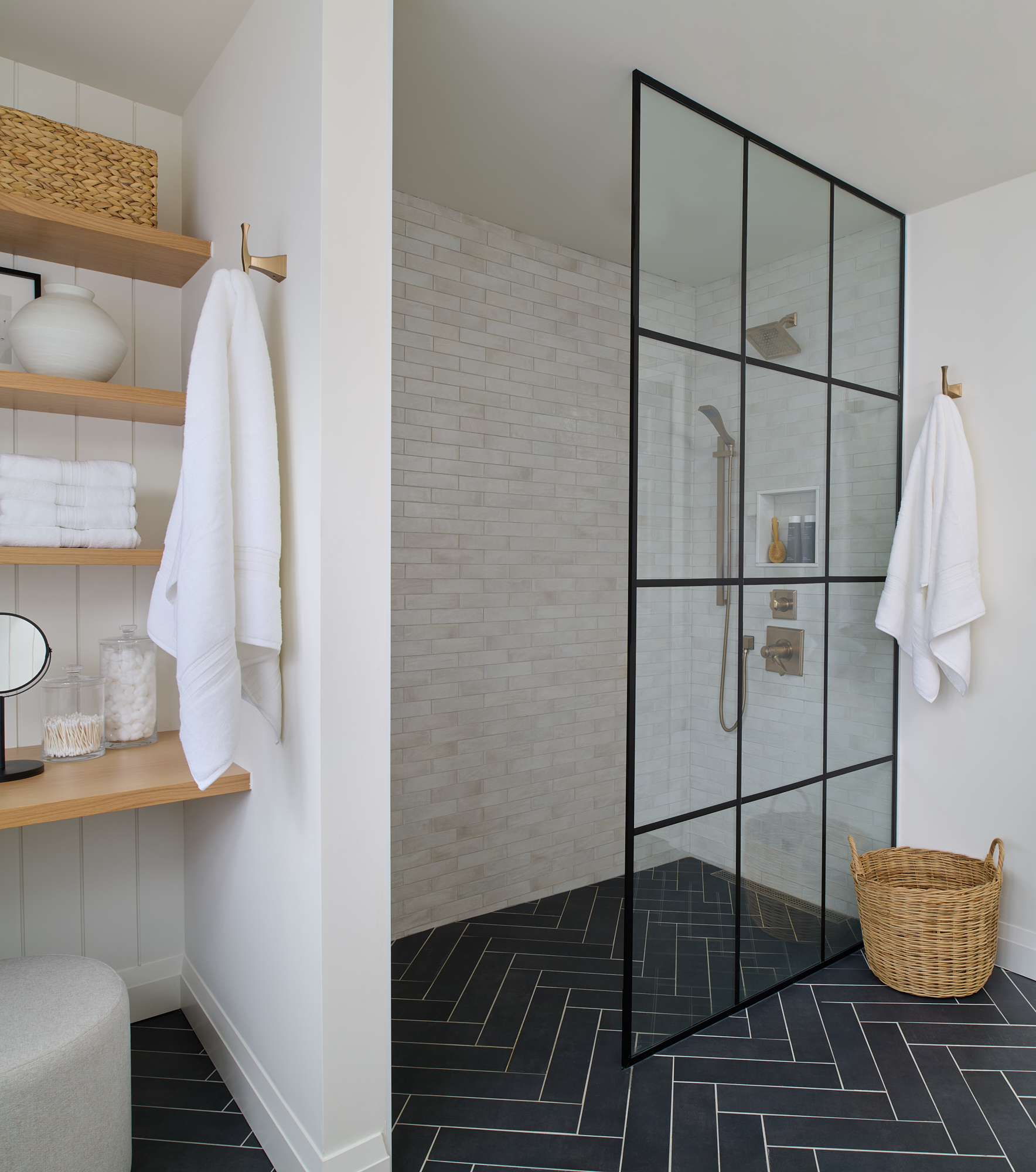 bathroom interior designed with black herringbone floor tile, subway tiled wall and shower glass with black iron frame 