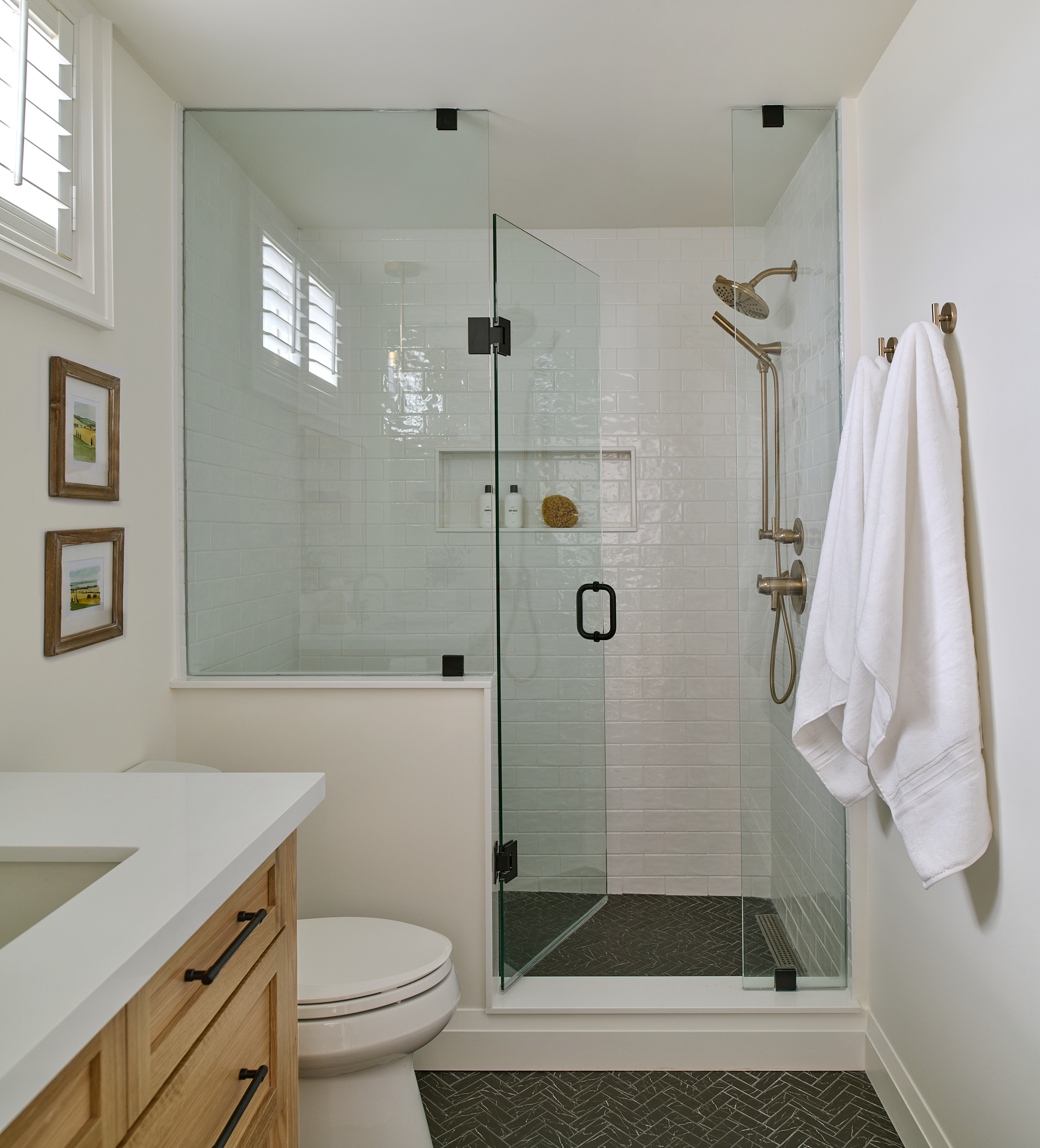 bathroom interior designed with oak wood vanity, gold plumbing fixtures and black herringbone floor tile