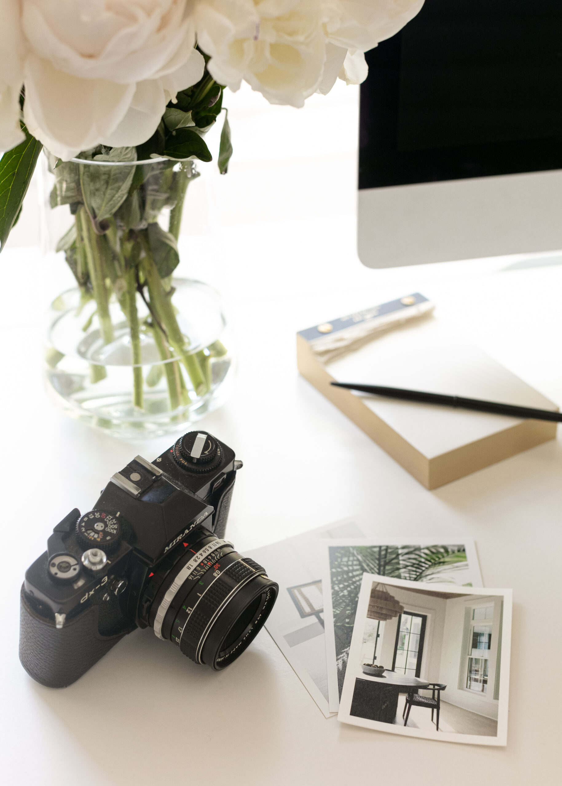 business owner's desktop with a camera, photos, note pad, monitor and vase with flowers