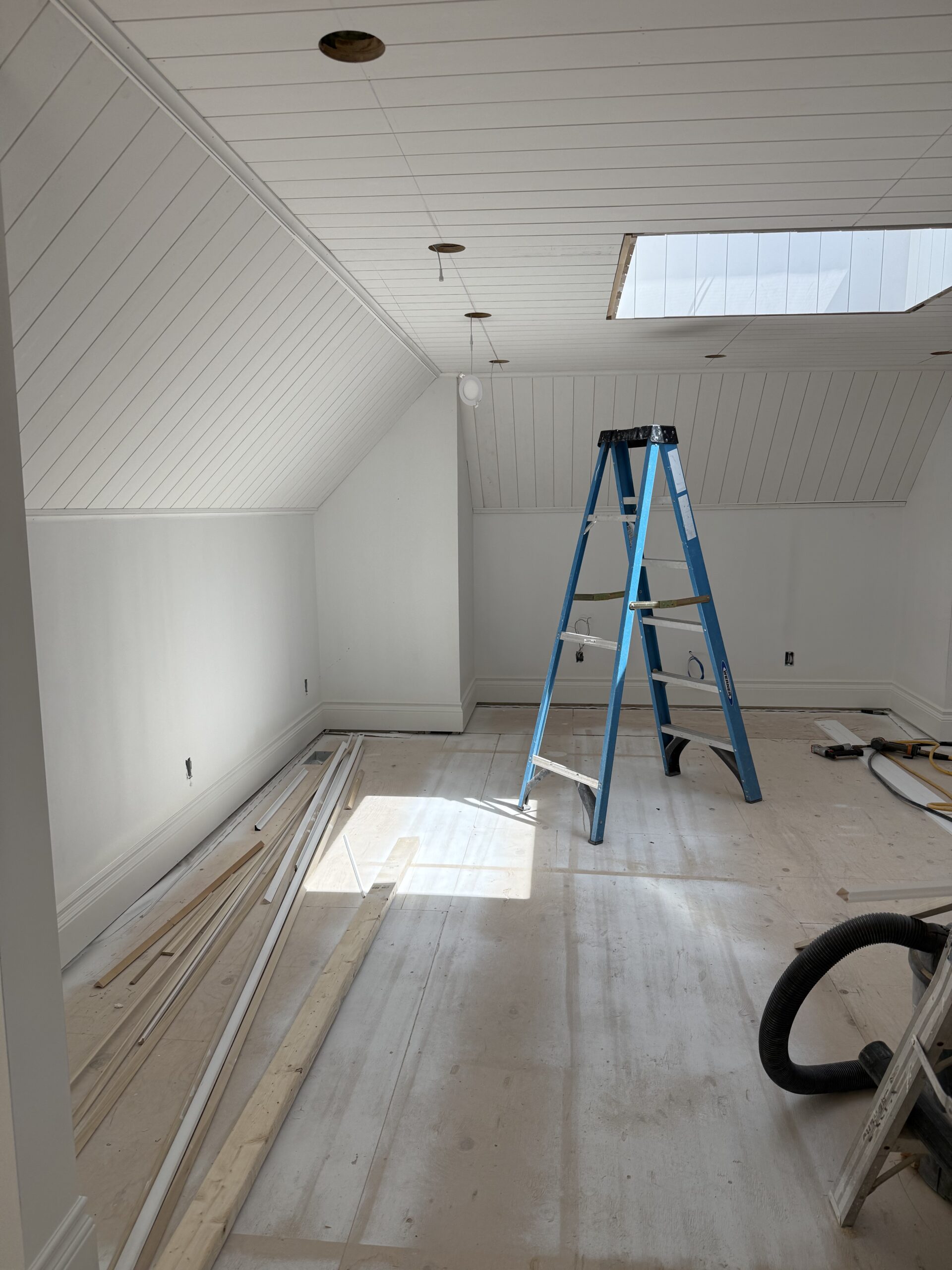 Attic renovation in progress featuring sloped shiplap ceiling and natural light from skylight