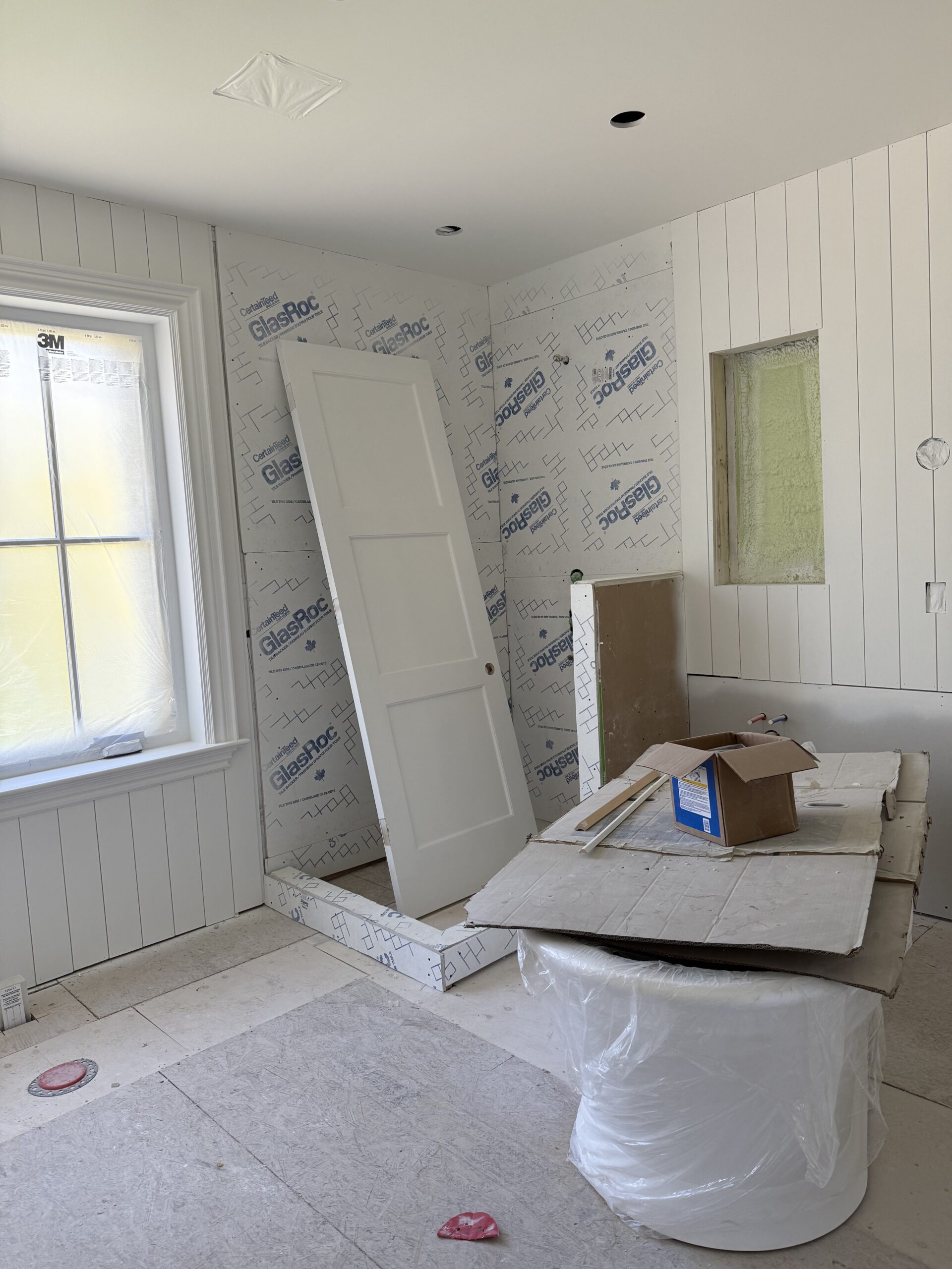 Primary bathroom renovation in progress featuring panelled walls, custom shower, and freestanding tub awaiting installation