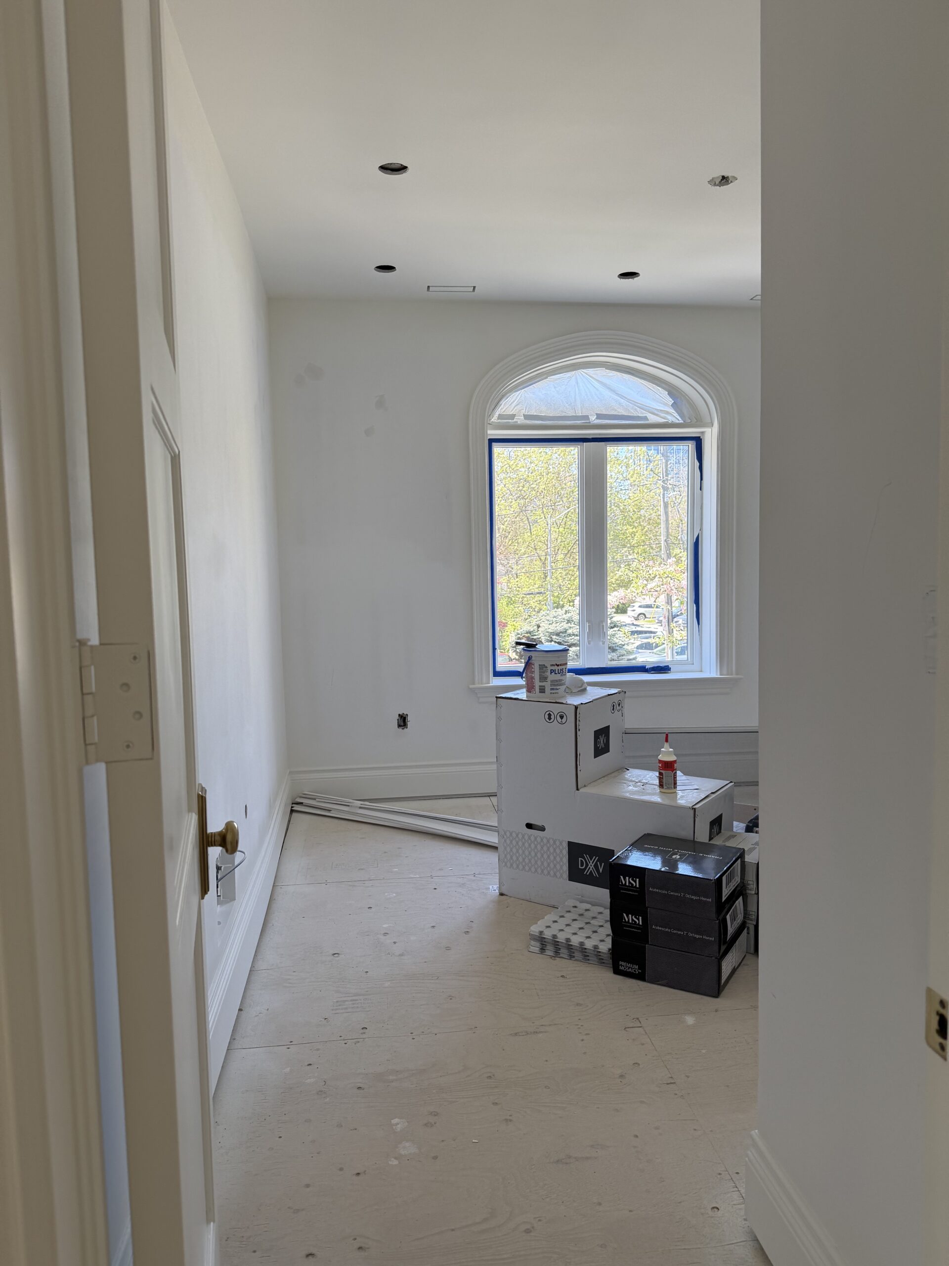 Upper floor bedroom under renovation with arched window and construction materials on site